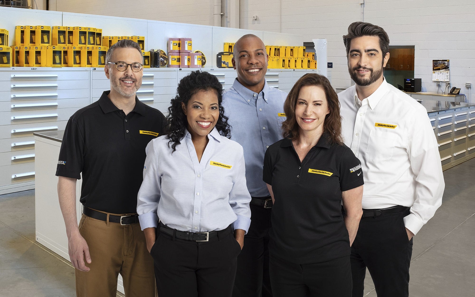 Group of Stanley Black & Decker representatives standing in a storage solutions showroom with industrial cabinets and yellow tool storage units in the background.