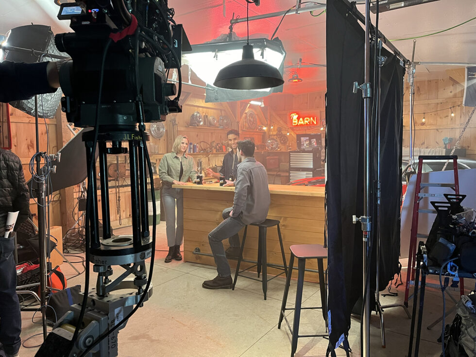 Film crew shooting the WIX TV spot inside a garage-style set, with camera rig and lighting equipment framing three actors at a wooden bar.