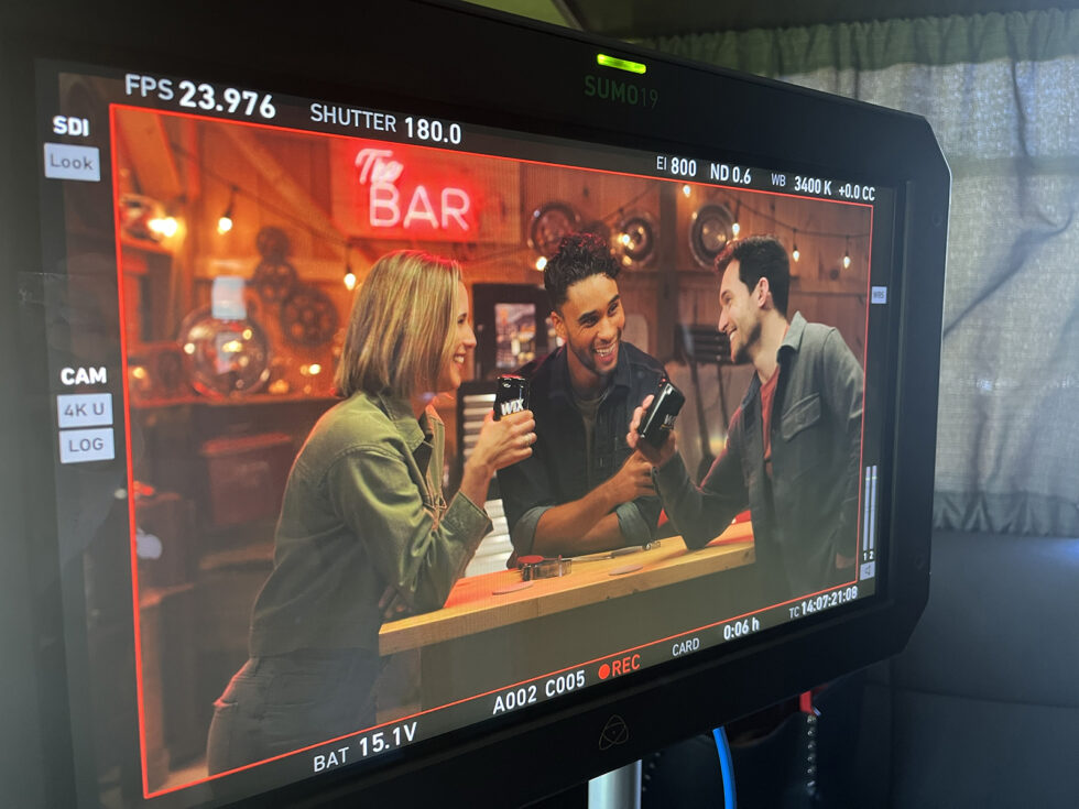 Monitor view of three actors toasting WIX-branded cans during filming of the national TV commercial.